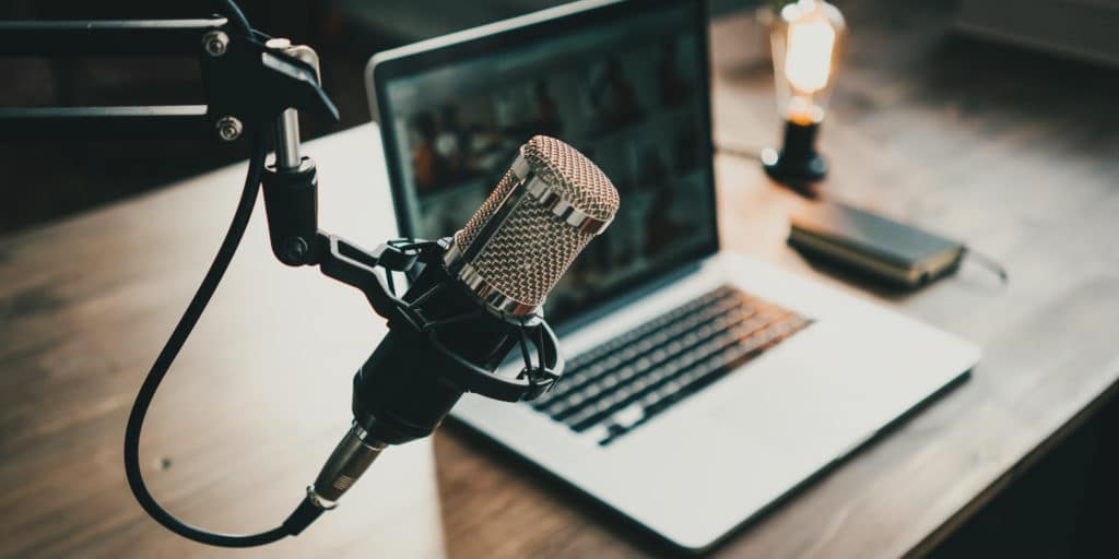 Aufnahme eines Podcast Set-ups mit einem Mikrofon im Vordergrund, Laptop und Smartphone im Hintergrund.